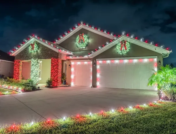 Ranch home with red and white roofline lights and wreaths over both garage doors
