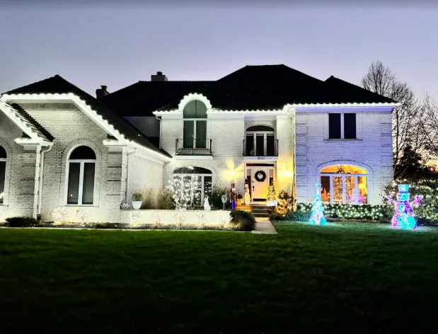 Estate home with warm white roofline lights and a lit front walk